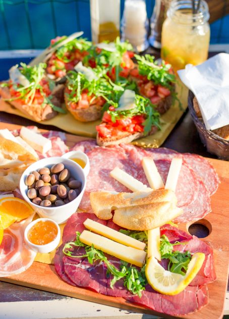 Tasty italian food. Fresh bruschettes, cheeses and meat on the board in outdoor cafe with amazing view in Manarola, Italy Tasty italian snack. Fresh bruschettes, cheeses and meat on the board in outdoor cafe with amazing view in Manarola